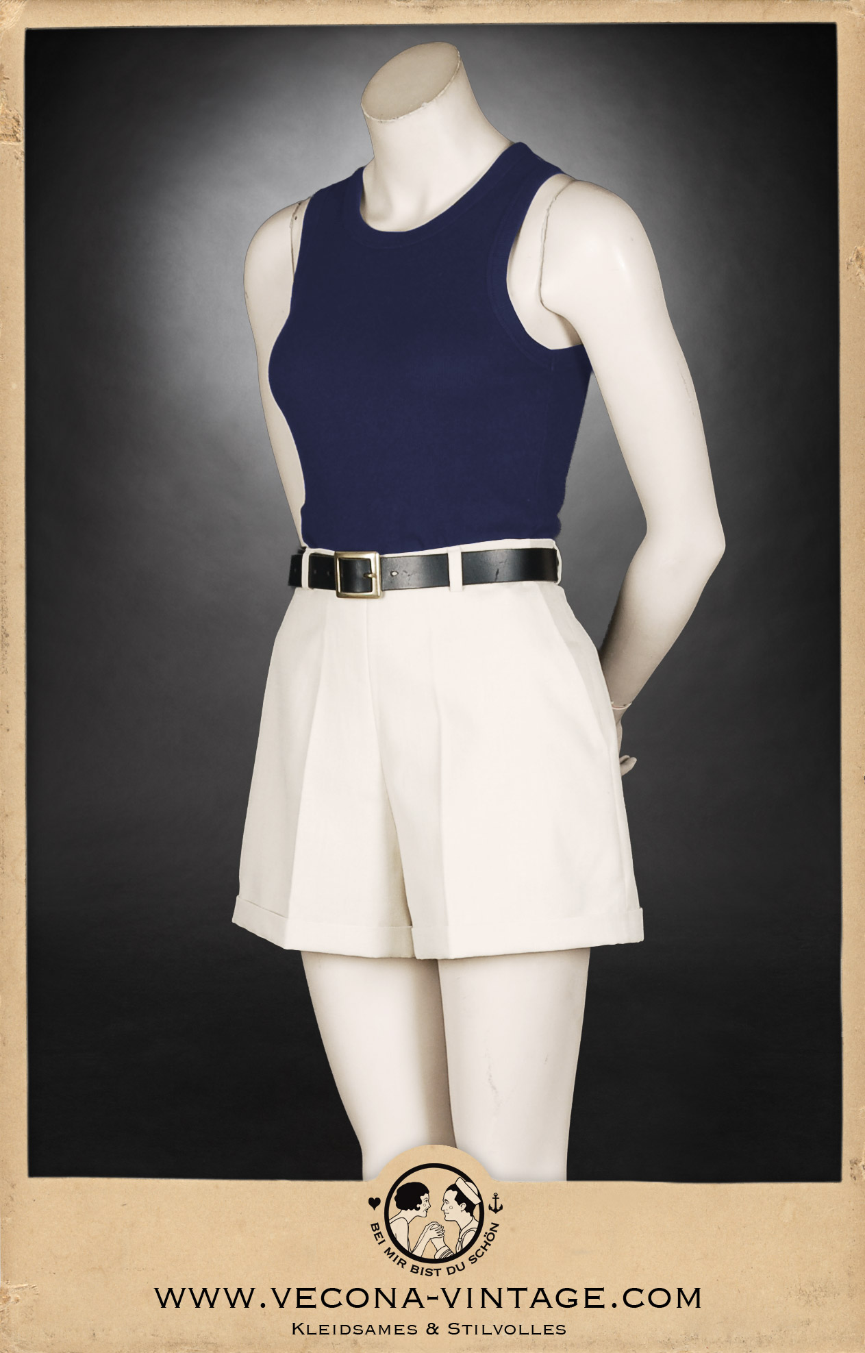 Sportliches 1930er Jahre Damen-Outfit mit hoch taillierten ecrufarbenen Leinenshorts und einem marineblauen Tanktop, akzentuiert durch einen schwarzen Ledergürtel – perfekt für Wassersport, Tennis oder Freizeit im Vintage-Stil.