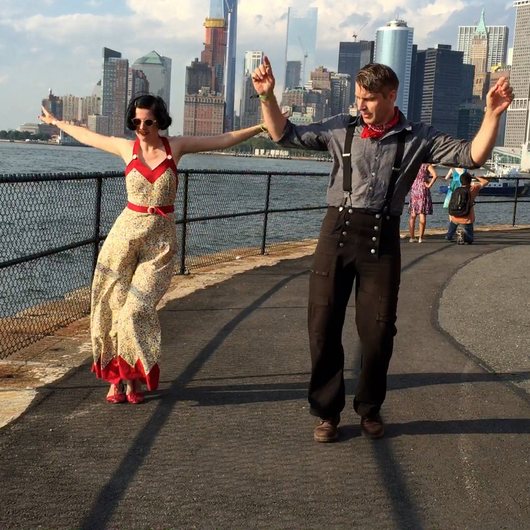 Swing Tanzen der Big Apple Routine in Vecona Vintage Mode mit der Manhatten Skyline im Hintergrund zur schönsten goldenen Stunde. Die Personen tragen Vintage Reproduktionen von Vecona Vintage.