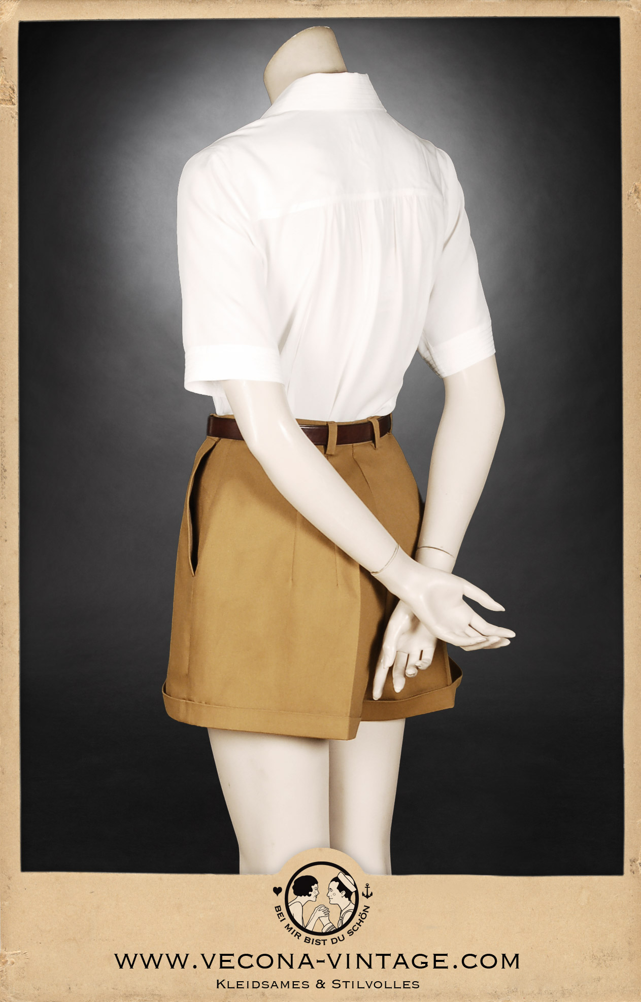 Klassische 1940er Jahre Damen-Shorts in Camel-Braun mit hohem Bund, weitem Bein und markanten Saum-Aufschlägen, kombiniert mit einer weißen Bluse und Ledergürtel. Ansicht der Rückseite.
